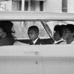 vintage photograph of six people in car, child in back seat is making eye contact with the camera