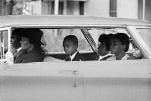 vintage photograph of six people in car, child in back seat is making eye contact with the camera
